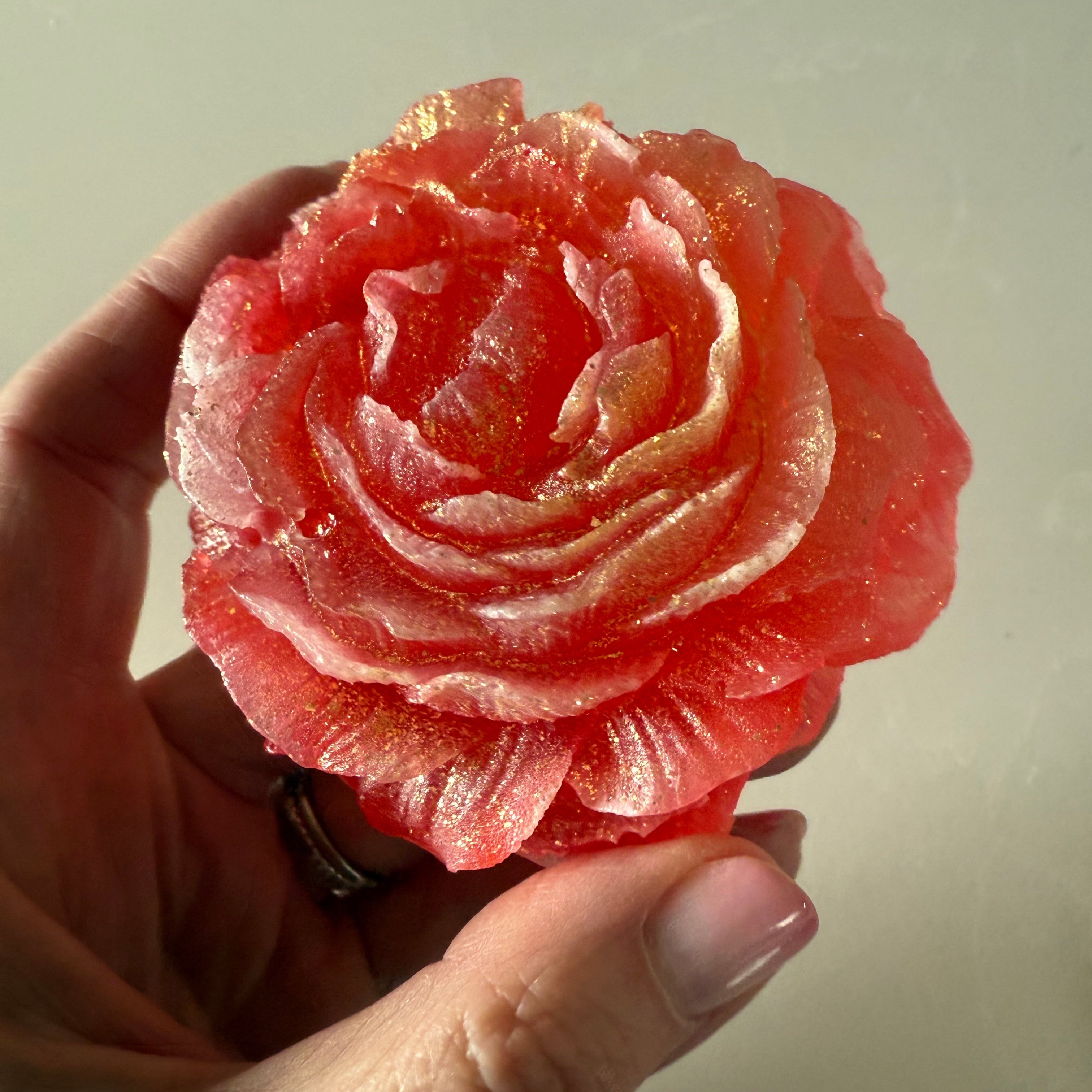 Hand holding a pink rose-shaped candy against a neutral background