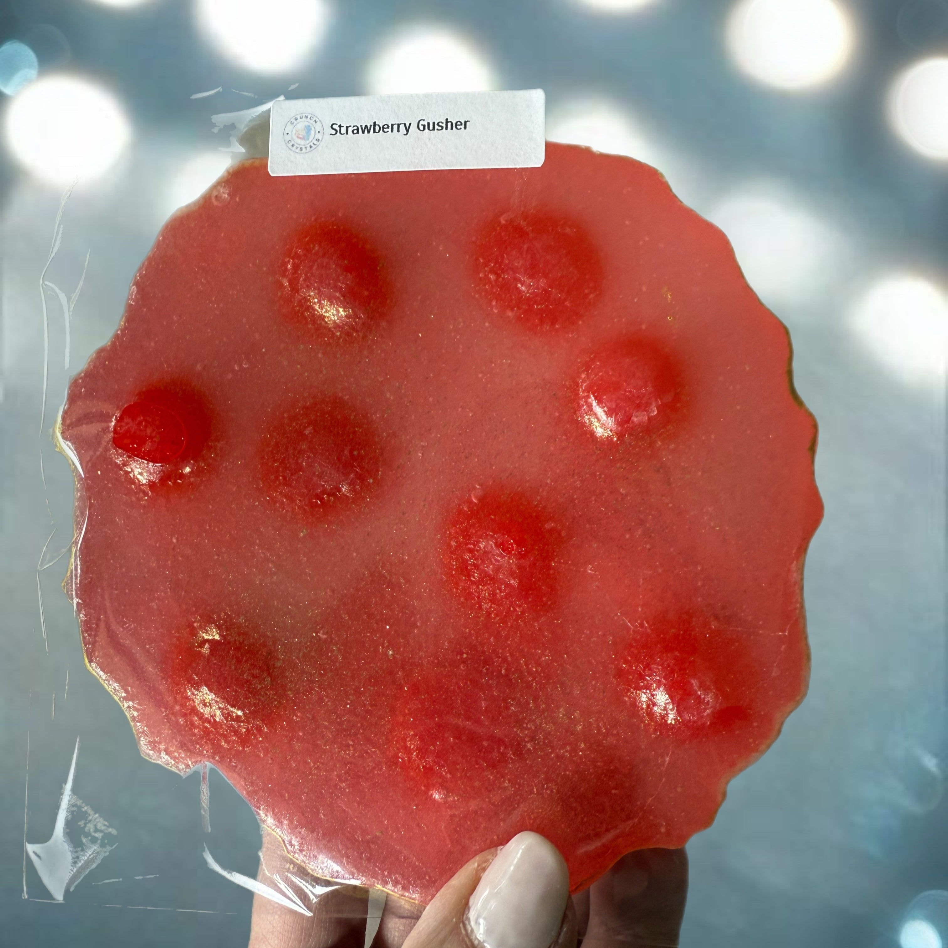 Red gummy bear-shaped candy held by a hand with a blurred light background