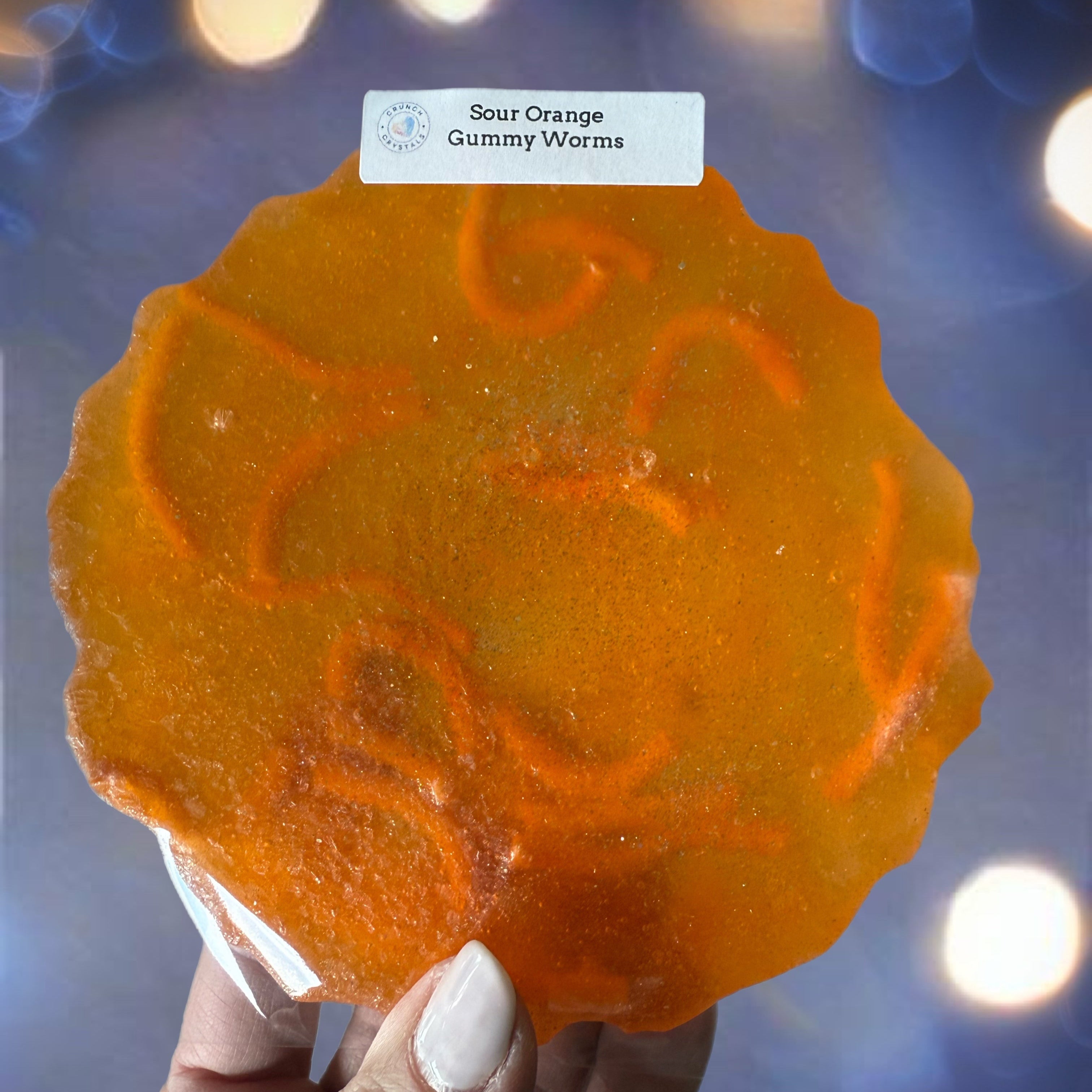 Orange gummy worm candy held by a hand with a blurred light background