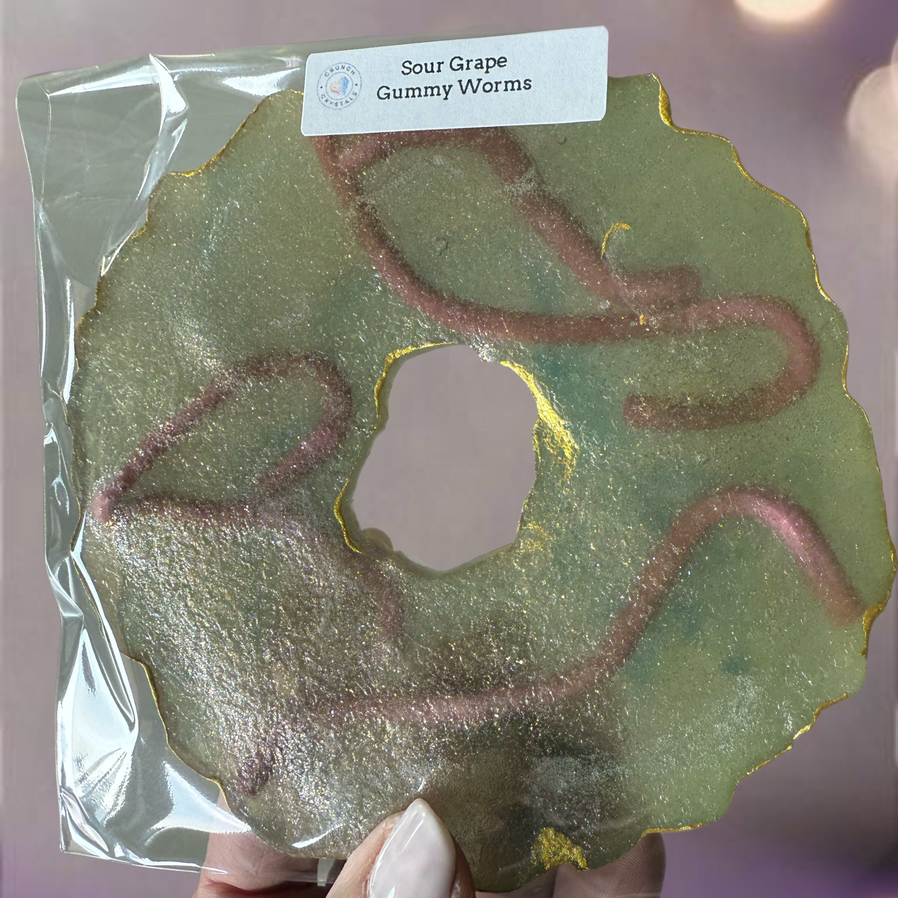 Packaged Sour Grape Gummy Worms with a hand holding it against a blurred background