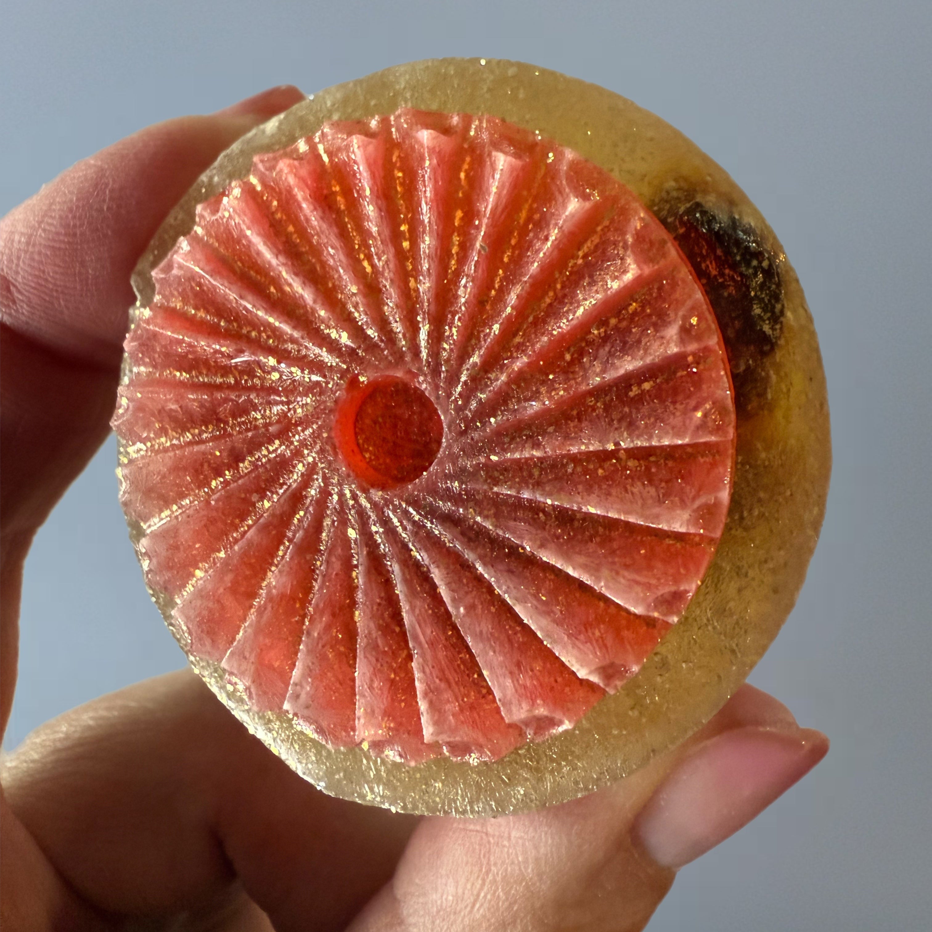 Close-up of a crystal candy with a decorative pattern held by a hand against a neutral background